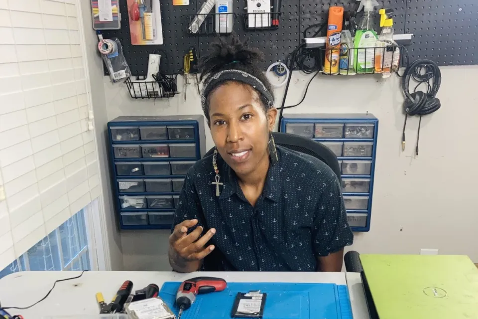 A Black woman works in a shop to prepare electronics for recycling..